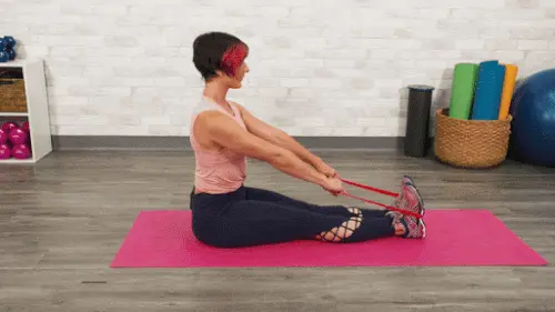 زن ورزشکار در حالت نشسته در حال اجرای حرکت قایقی با کش تمرینی برای عضلات پشت و بازو